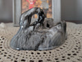 A glossy black and white marbled figurine shaped like a curled-up animal or creature, displayed on a translucent white petal-shaped stand in a tabletop setting.