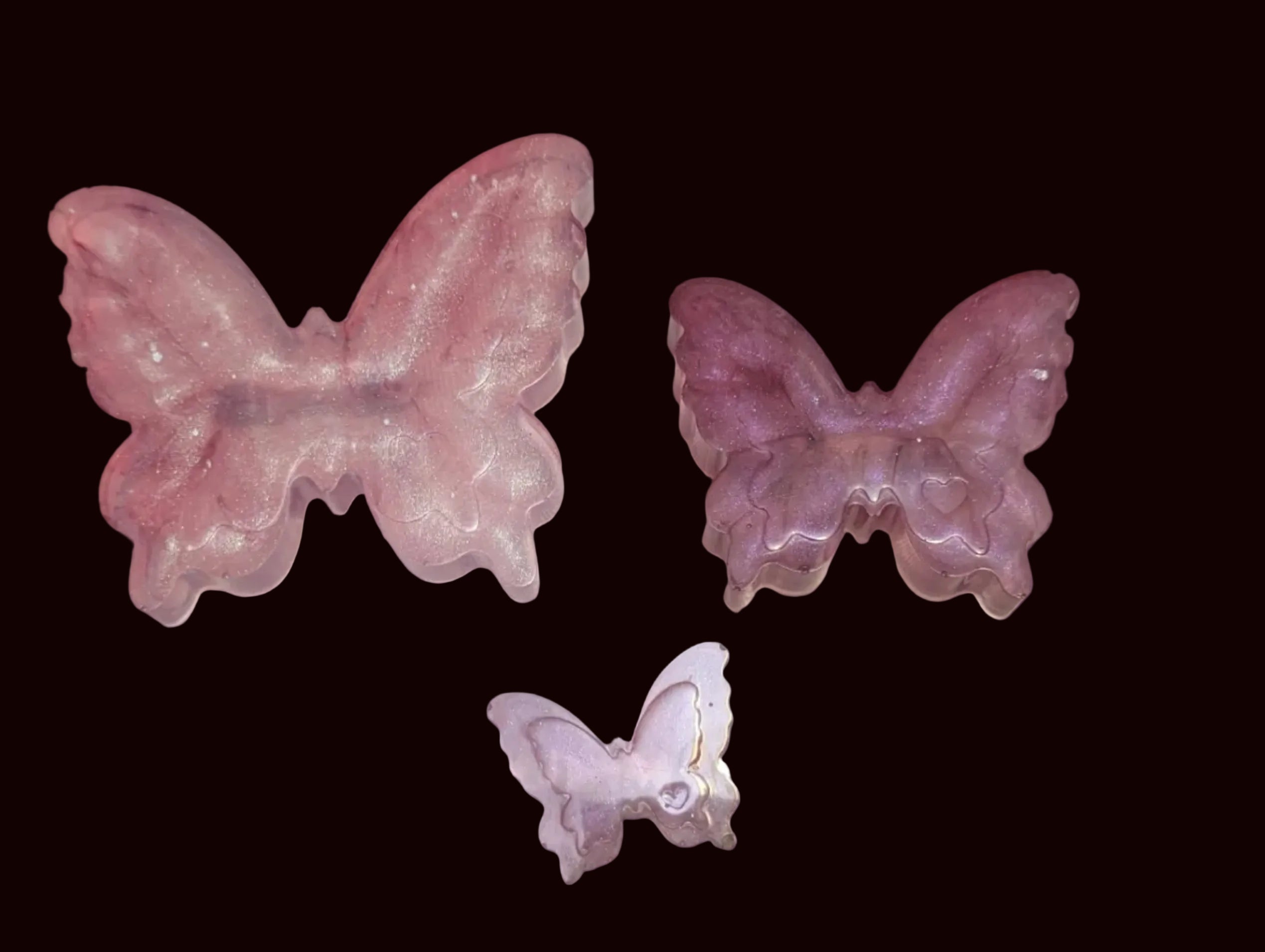 Three carved butterfly-shaped jewelry pieces in pink, mauve, and lavender.
