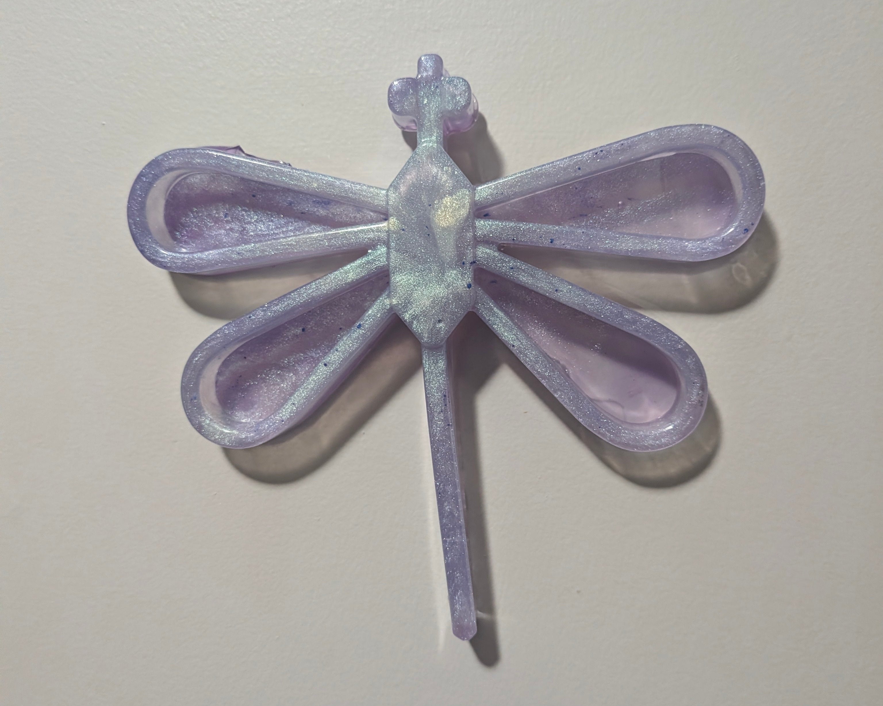 Handcrafted Dragon wall decor one-of-a-kind resin ethereal shimmer. Poured in a dreamy lavender purple with an iridescent glow, the glossy finish catches the light and adds a soft magical vibe to any wall. As a fully handmade piece, it has a tiny imperfection that makes it uniquely yours, part of the charm and proof that no two are ever alike. Perfect for brightening up a nursery, office, or any space that could use a pop of color and fantasy. 