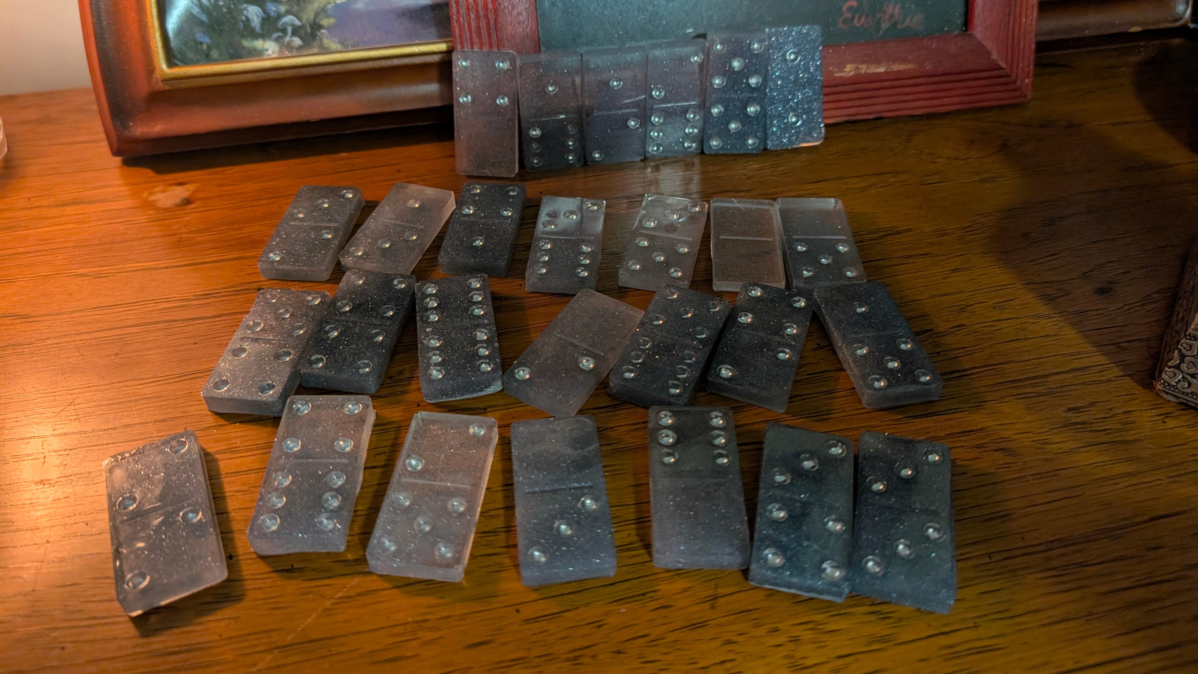 Handcrafted smoky gray with subtle sparkle resin domino set- 28 pieces make a statement with this moody, smoky gray set poured in rich smoky gray resin with a subtle sparkle throughout Each of the 28 full size dominos feature bright silver pips that catch the light beautifully against the deep gray, giving them an almost starry night feel. The glossy finish is smooth to the touch, and the marbled effect means every set is one of a kind. Perfect for game night or as a collector's piece that doubles as decor.